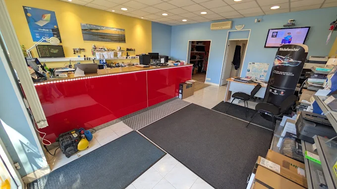 Intérieur de la boutique : comptoir d’accueil rouge, matériel informatique et pièces détachées